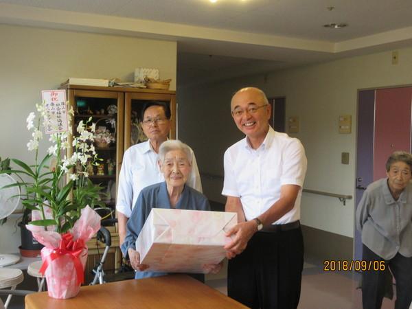 市長が長寿御祝の訪問の際に松本マツヱさん(104歳)へ御祝の花と記念品を贈呈している写真