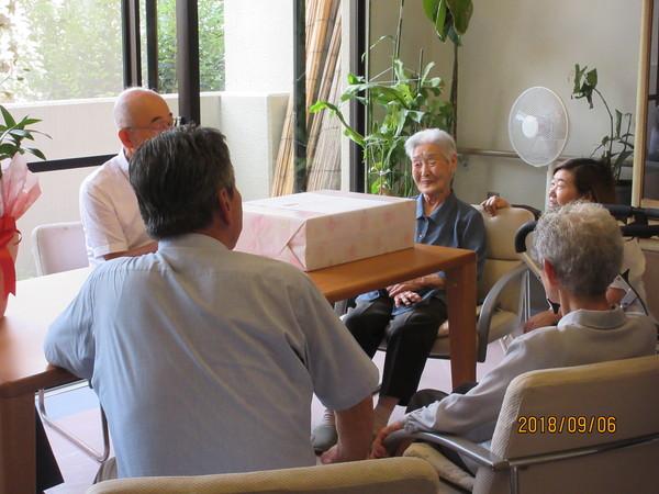 市長が長寿御祝の訪問の際、御祝の花と記念品を前に松本マツヱさん(104歳)と談笑している写真