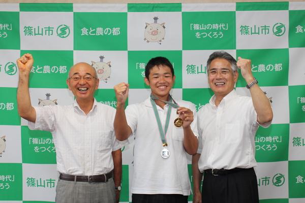 市長と教育長の間に松葉君が立って、3人でガッツポーズをして笑顔で写っている写真