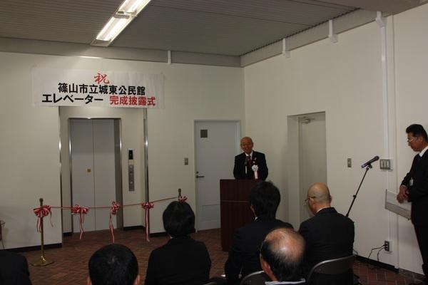 エレベーターの前に設置されたテープカットリボンと、その横で話をしている市長の写真