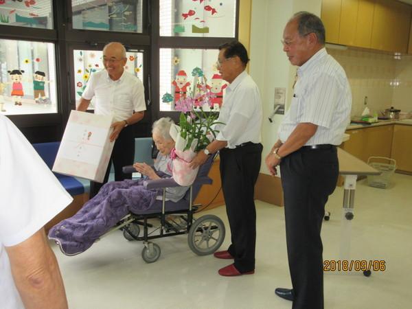 車いすに座っている岸本冨子さん(106歳)と長寿御祝の記念品を持った市長らとの写真