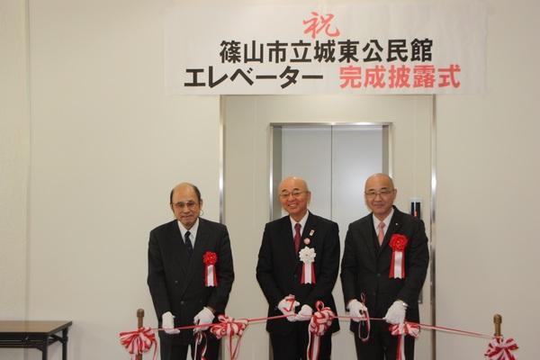 エレベーターの前で、テープカットをしている市長と男性2名の写真