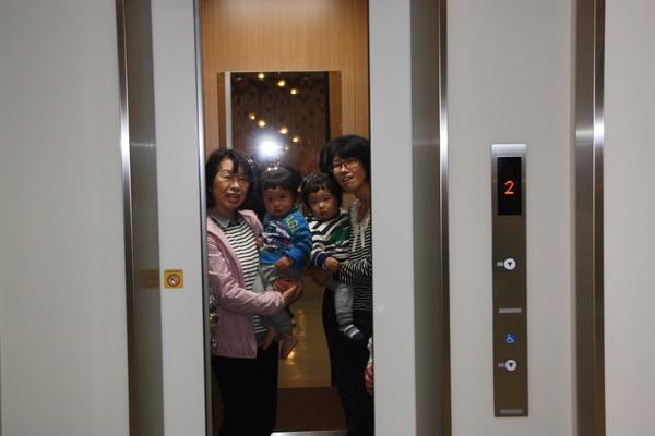 エレベーター内で、小さい子供を抱く女性2名の写真