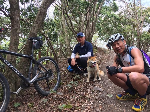 山中で犬を連れた市長と、自転車で登ってきたヘルメットをかぶった男性がしゃがんでいる写真