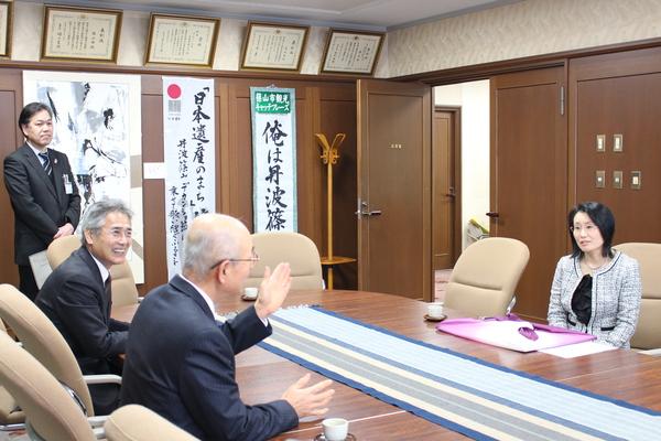 市長と酒井 美奈子先生が向かい合って座り、市長が酒井 美奈子先生に身振り手振りで話をし、横にいる男性が笑顔で話しを聞いている様子の写真