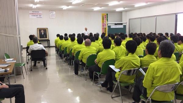黄緑色のシャツを着て着席する関係者と、その前で話をする市長の写真