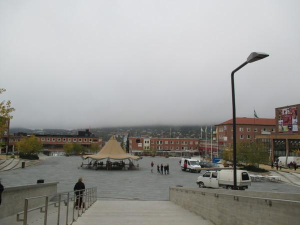 曇り空の下、広場にテントが設置されていてその周りに白い車が停車している近くで数人の人がいるのを広場におりる階段の上から全体をうつした写真