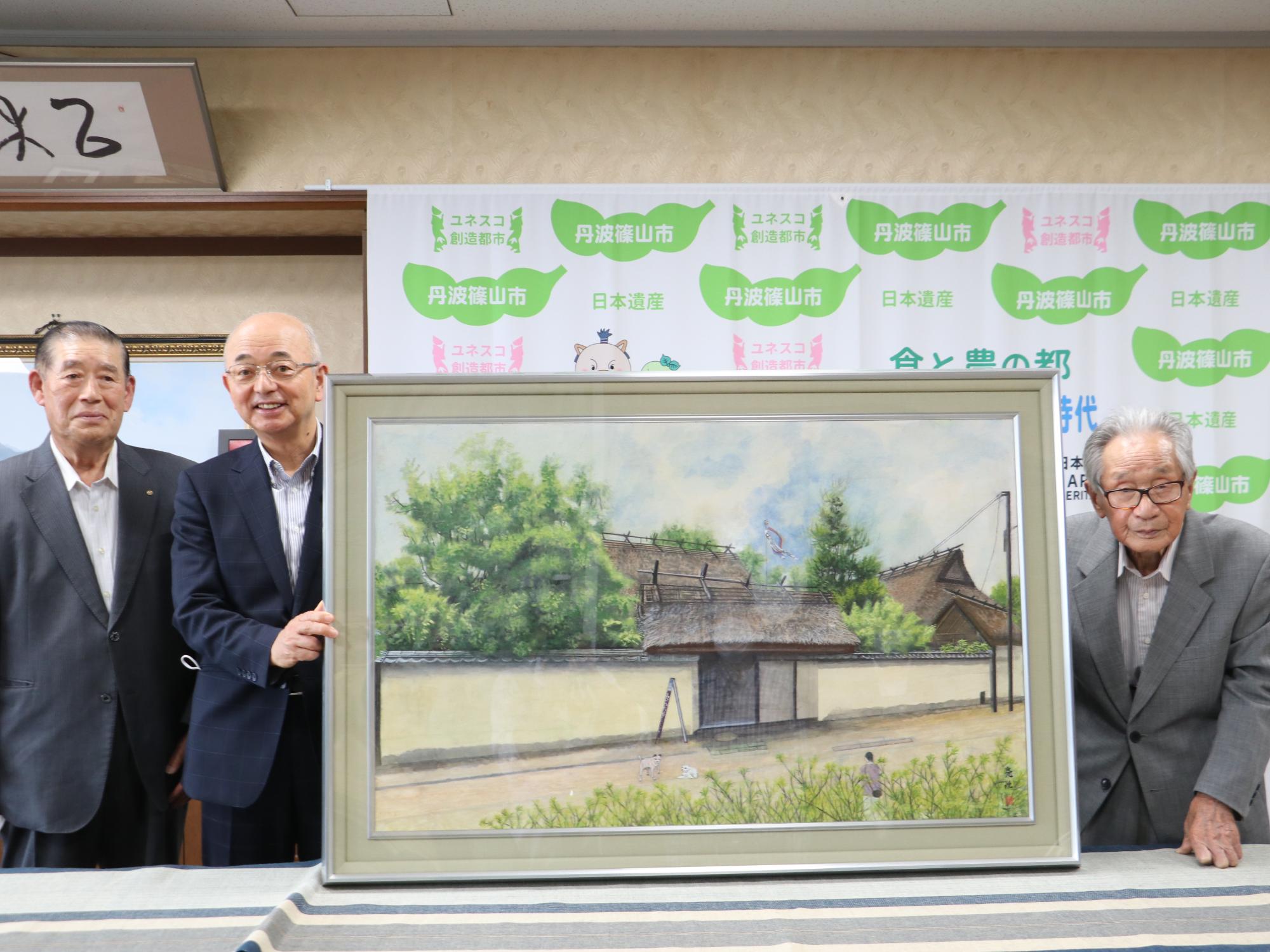 武家屋敷を描いた日本画の右隣に男性が一人、左隣に男性が二人立っている