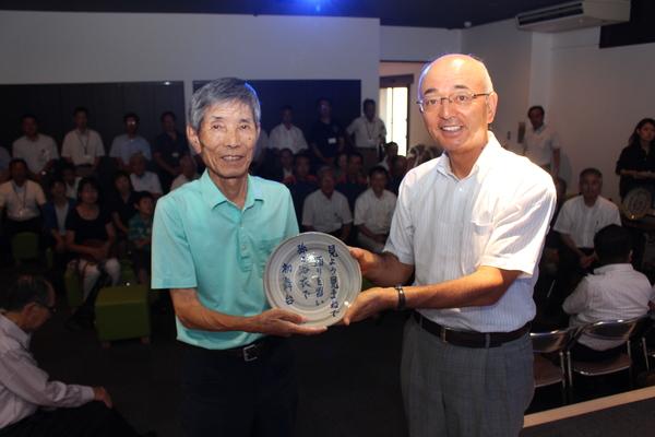 御崎さんと市長が、御崎さんのデカンショ節「見よう見まねで踊りを習い孫が浴衣で初舞台」が書かれたプレートを一緒に持っている写真