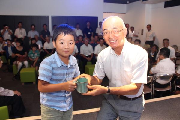 こども賞の長澤くんが、市長と一緒に陶器の青緑色のマグカップを持っている写真