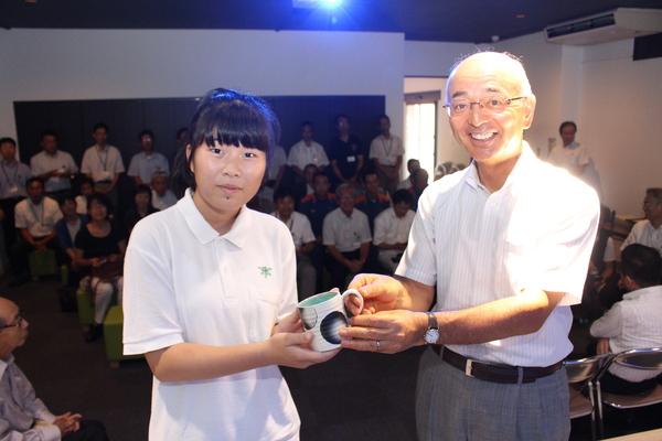 若者賞の井上さんが、市長と一緒に陶器の白地に黒の丸が書かれたマグカップを持っている写真