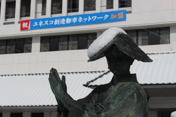 女性の銅像の編み笠の右側に雪が積もつている写真