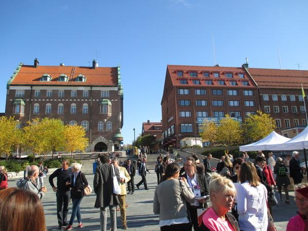青空の下、街にはたくさんの人がいて周りは大きな建物に囲まれている写真