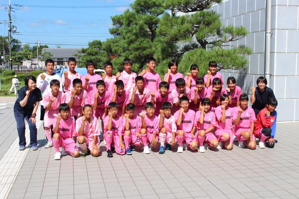 ピンク色のユニフォームを着た篠山丹南ホッケー部の部員と関係者が、右手でガッツポーズをして3列に並んで写っている集合写真