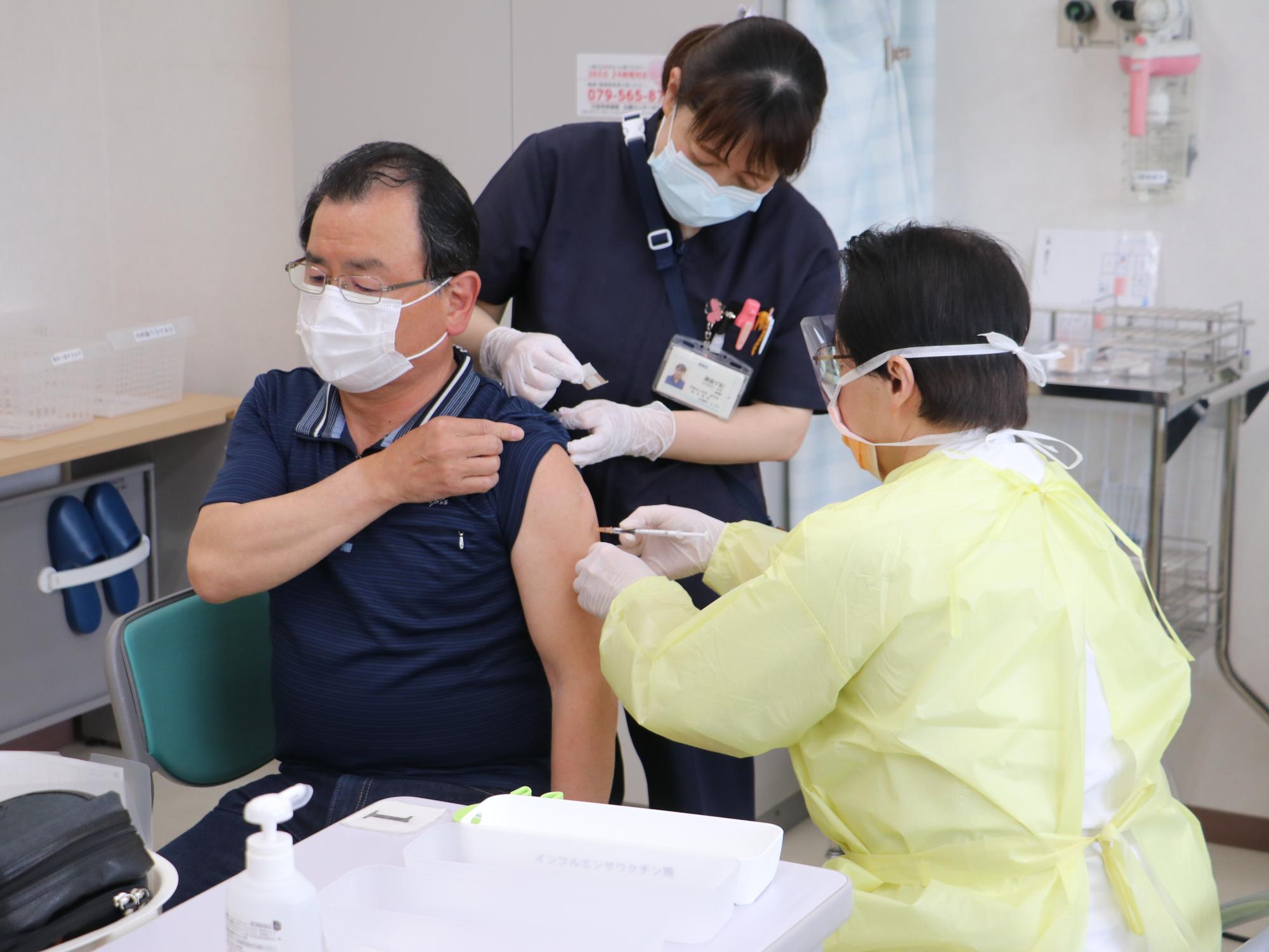男性がポロシャツの袖をめくってワクチン接種を受けようとしている。