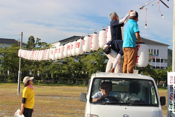 男性が、軽トラックの荷台に乗り、提灯をつけている写真