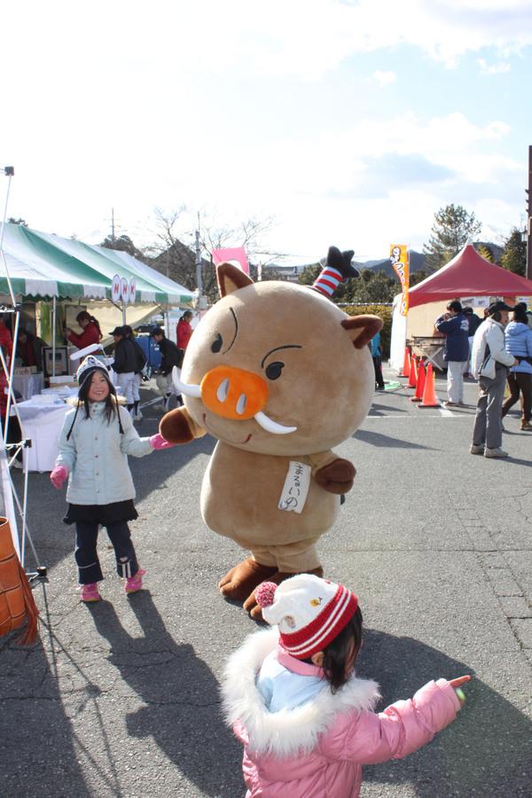 まるいのの着ぐるみと、防寒用の帽子とジャンパーを着た女の子が手をつないで立っている写真