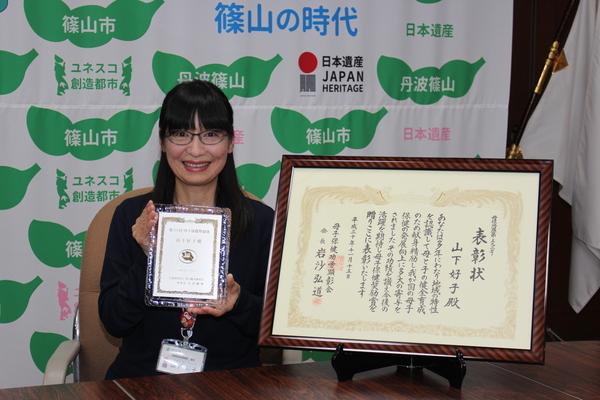 額に入った賞状の横で、記念の盾を持った山下さんがニッコリと微笑んでいる写真