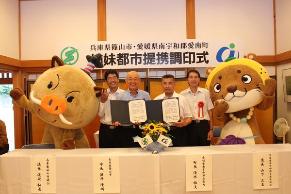 まるいのの着ぐるみとタヌキの着ぐるみの間に市長と3人の男性が立っている写真