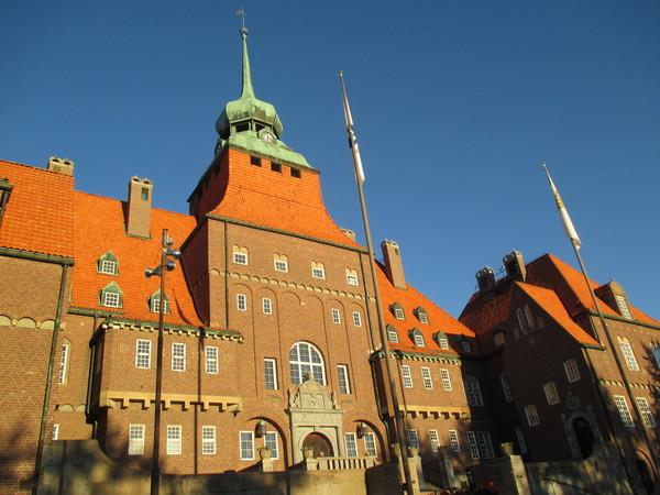 屋根がオレンジ色でその上がみどりっつぽくなっている塔のようなところに時計がある市役所をうつした写真