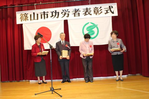 壇上で受賞者男性1名、女性3名が賞状の入った盾を持っている写真