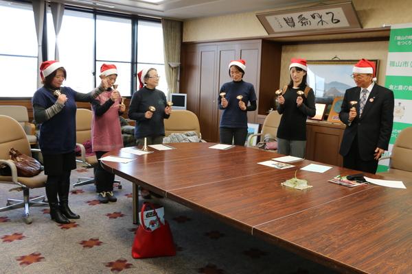 こんにちは市長室にてサンタ帽子を被った中野母親クラブの皆さんがハンドベルで「きよしこの夜」の演奏のプレゼントをしている写真