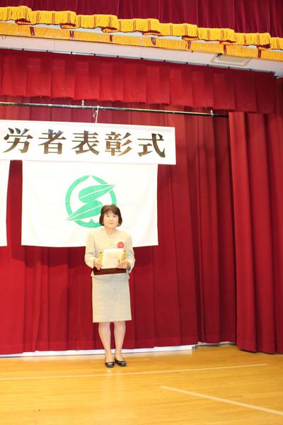 壇上で受賞者女性1名が賞状の入った盾を持っている写真