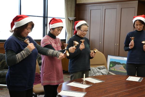 サンタ帽子を被った中野母親クラブの皆さんが両手にハンドベルを持ち、右手や左手を前に出し演奏している写真