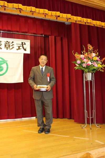 壇上で受賞者男性1名が賞状の入った盾を持っている写真