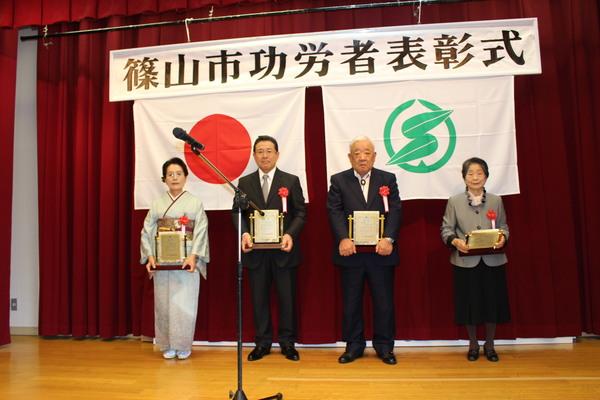 壇上で受賞者男性2名、女性2名が賞状の入った盾を持っている写真