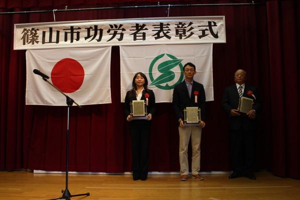 壇上で受賞者男性2名、女性1名が賞状の入った盾を持っている写真