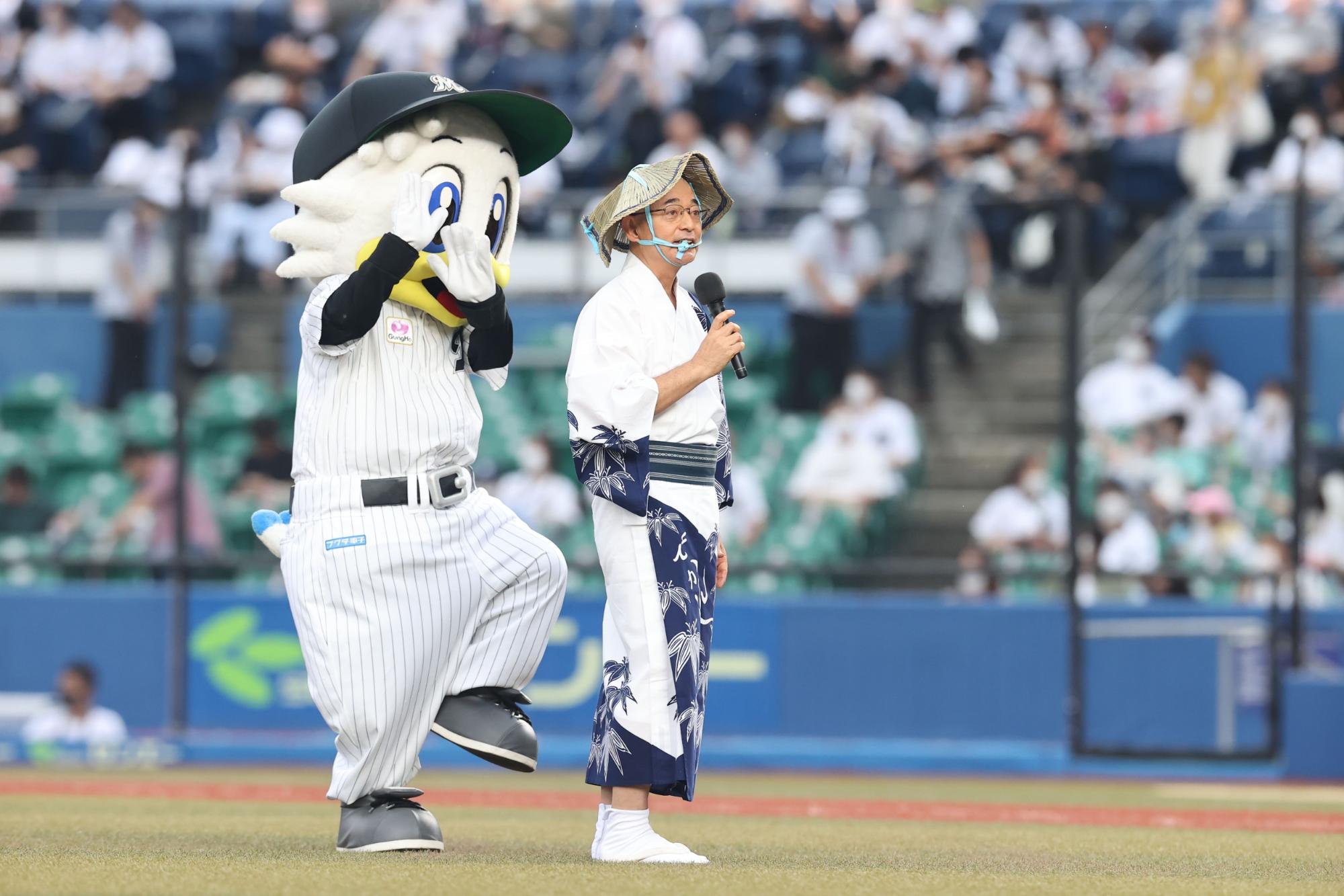 編み笠をかぶって、デカンショ浴衣を着た市長がマイクを持ってマウンドであいさつしている。隣には千葉ロッテのマスコット。