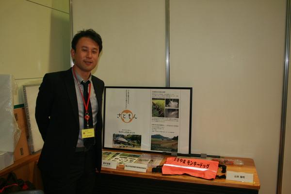 「さともん」を紹介している資料の前で鈴木 克哉さんが写っている写真