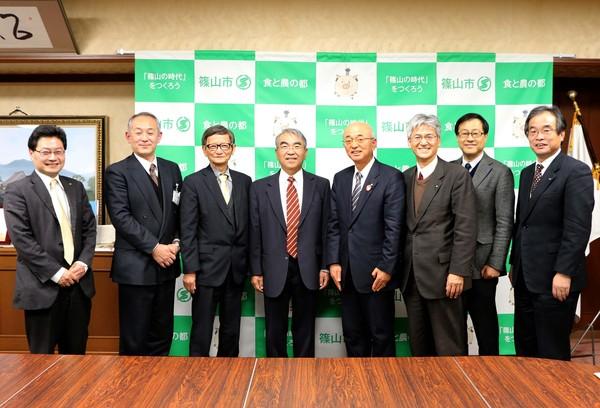 金出 武雄さんと酒井市長が真ん中に立っており、その両脇に3人ずつ職員が立っている写真