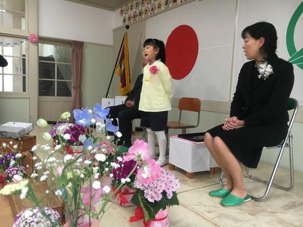 舞台の上で、スーツを着た男性と女性の間に立っている卒園生の松宮 朱利さんの写真