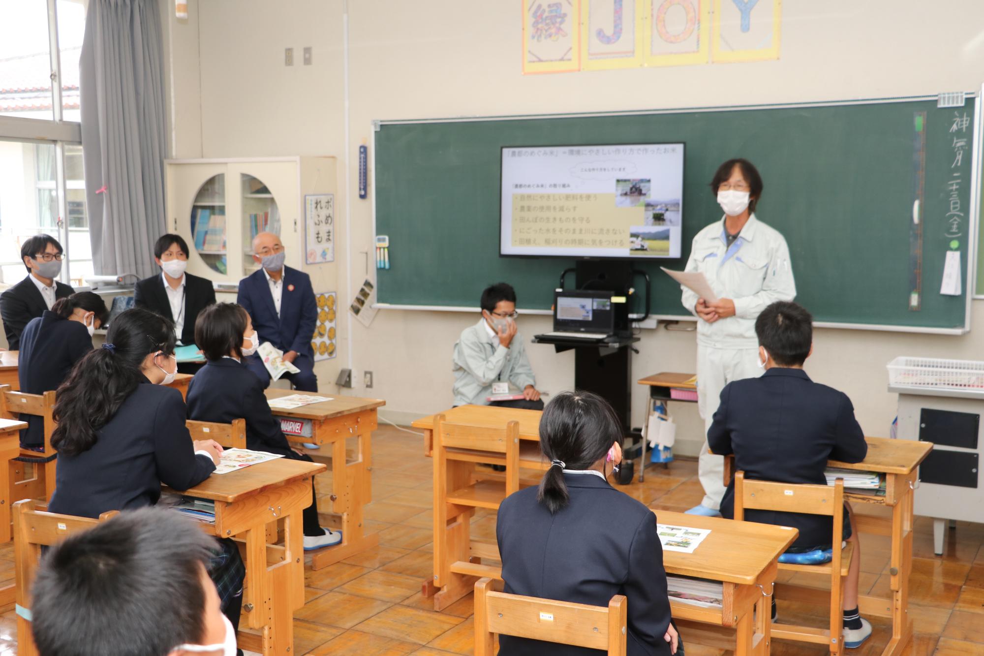 生産組合の辻井さんがプロジェクターを使って子どもたちに説明している