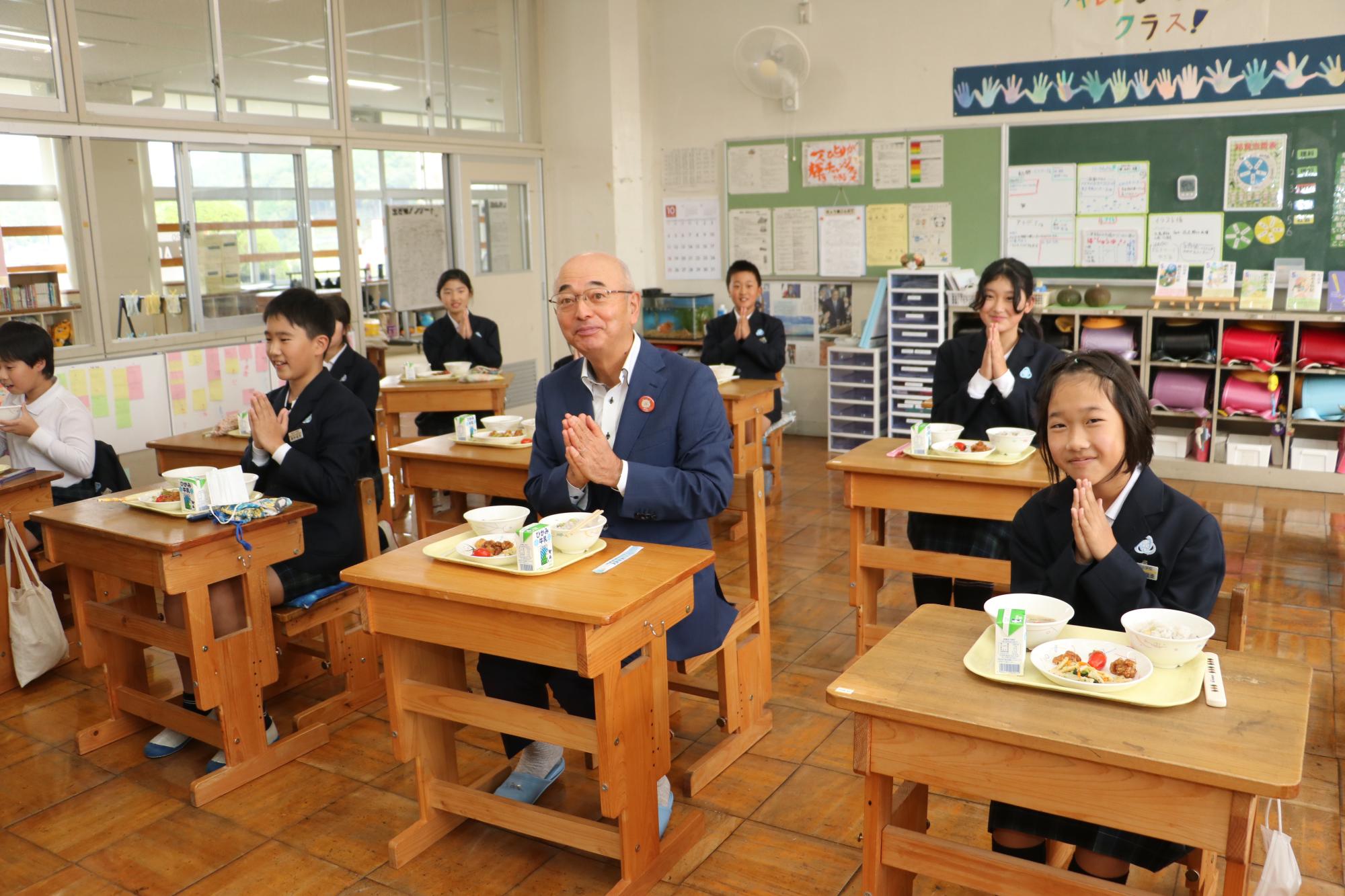 市長と子どもたちが机を並べて給食を食べようと手を合わせている