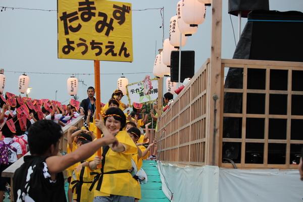 「たまみずようちえん」と書かれたプラカードを持った女性の後ろから子供達がついてきている写真