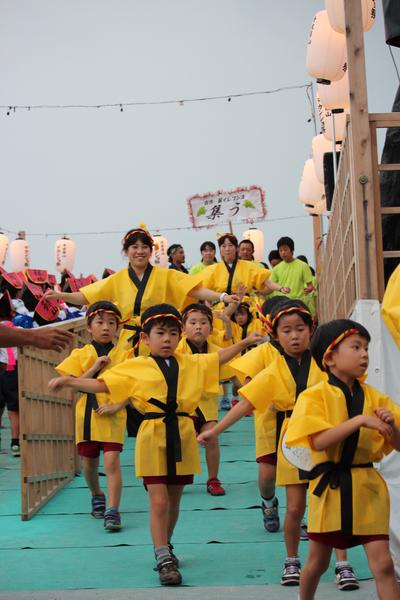 黄色に黒のラインがはいったハッピをきたたまみず幼稚園の園児と先生が踊りを踊っている写真