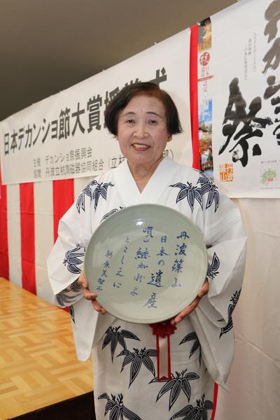 大賞を受賞した浴衣姿の杉原 美智子さんが「丹波篠山日本の遺産唄い継がれよとこしえに」と書かれた皿を持っている写真