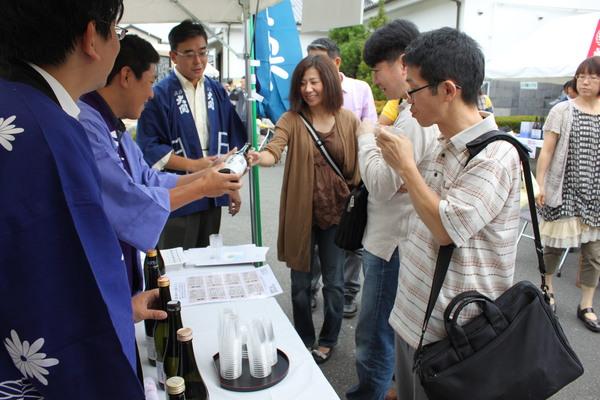 テントの中で法被を着た男性から来場者の女性がお酒を注がれている写真