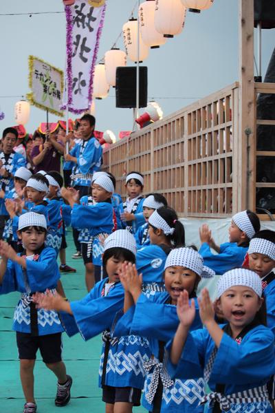 お祭りの法被を着た子供達が顔のところに手を持っていき踊っている写真