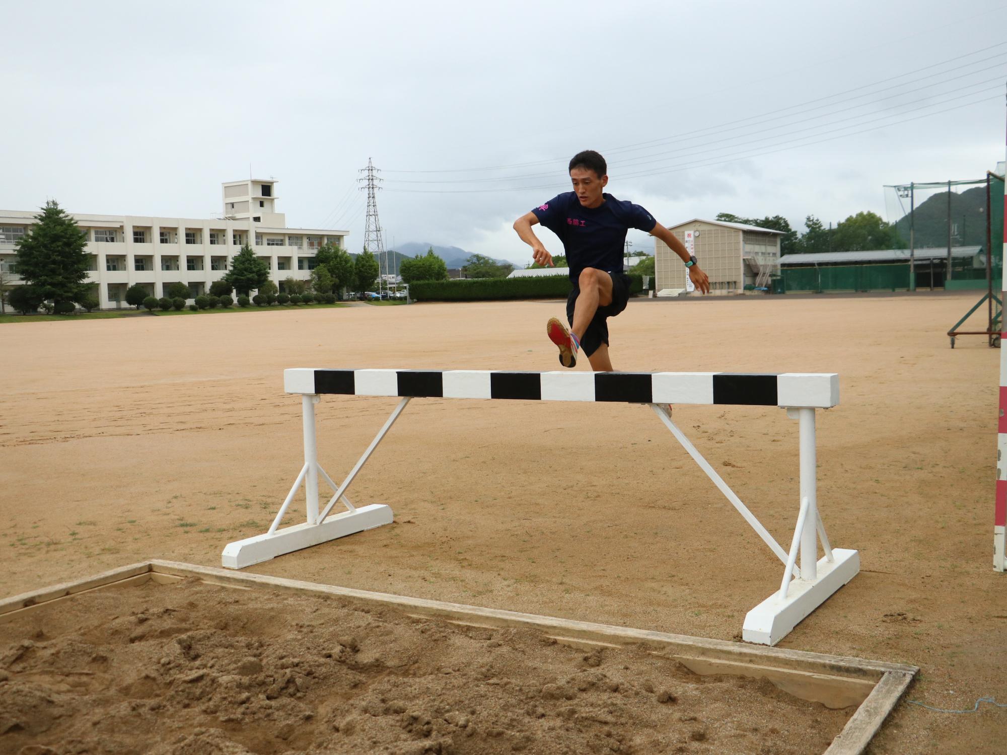 陸上部のユニフォームを着た男子高校生が走りながらハードルを跳んでいる