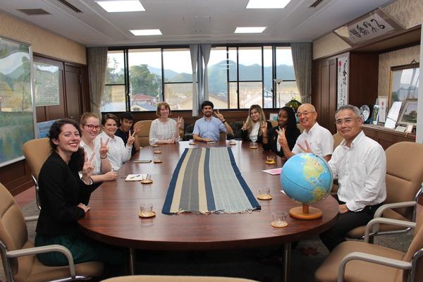 地球儀がのった楕円形のテーブルに着席してピースサインをしているALTの先生方の写真