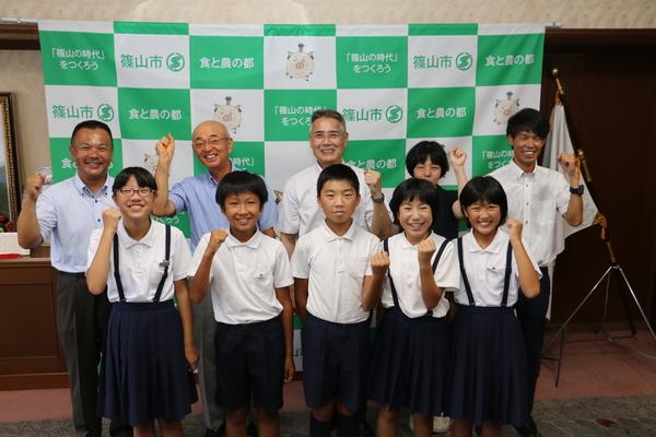 笑顔で、ガッツポーズをしている小学生の生徒たちと、市長、関係者の写真