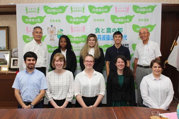 5人のALTの先生が横に並んで立っている前に5人のALTの先生が横に並んで座っている写真