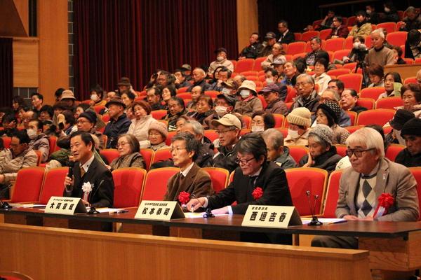 観客席の前に審査員席が設けられており、一番左奥審査員のがマイクを持って話をしており、その後ろの客席には沢山のお客さんが座っている様子の写真