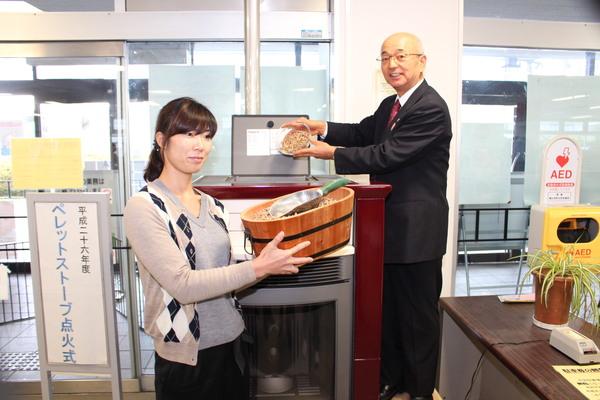 ペレットストーブに市長が点火剤を入れようとしていて布施 未恵子さんが容器に入った点火剤を持っている写真