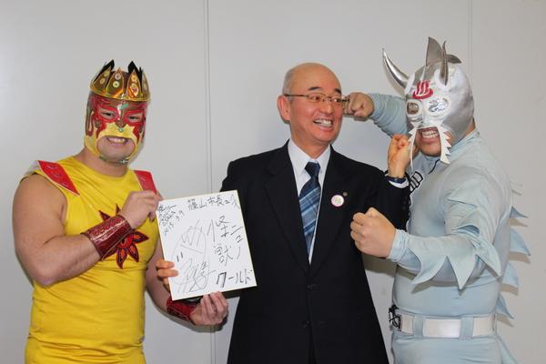 市長がニューワールドの顔にアッパーカットをしようとしており、ニューワールドは両手で拳を握ってポースをとり、タコヤキ―ダーはサインした色紙を持って写っている写真