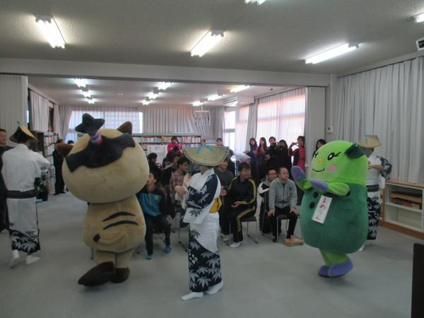 椅子に座った人たちの周りをまるいのの着ぐるみや着物を着た女性たちが踊っている写真